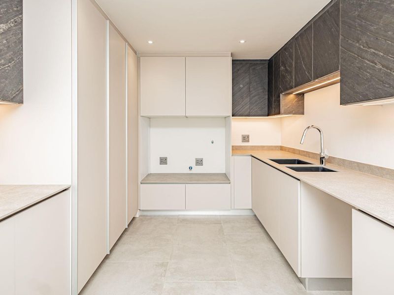 A modern, high-specification scullery featuring sleek handleless cabinetry, stone countertops, a double sink, and integrated under-cabinet lighting.