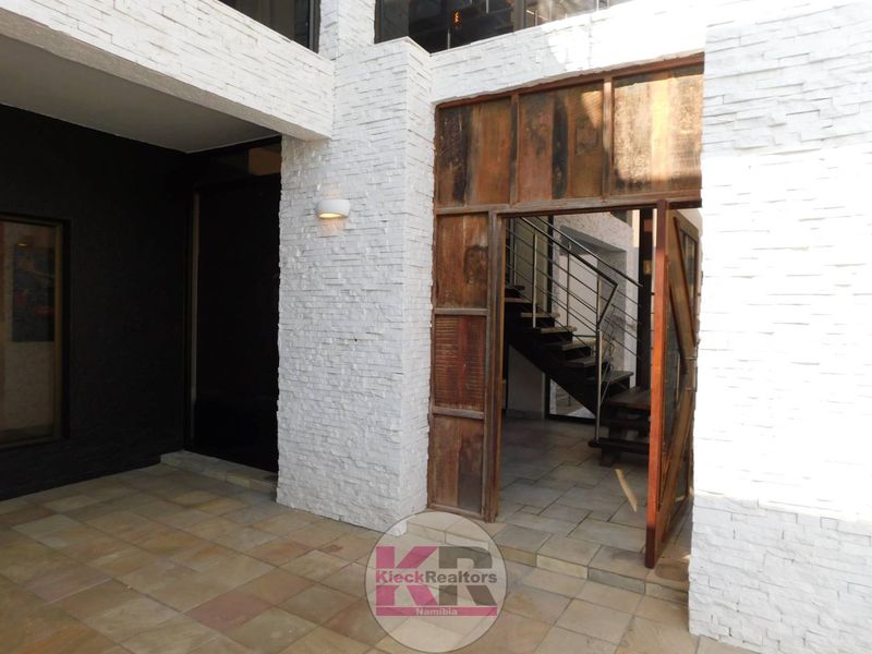 A covered patio area featuring stone-clad walls, tiled flooring, and a rustic timber door frame leading to an internal staircase with a stainless steel balustrade.