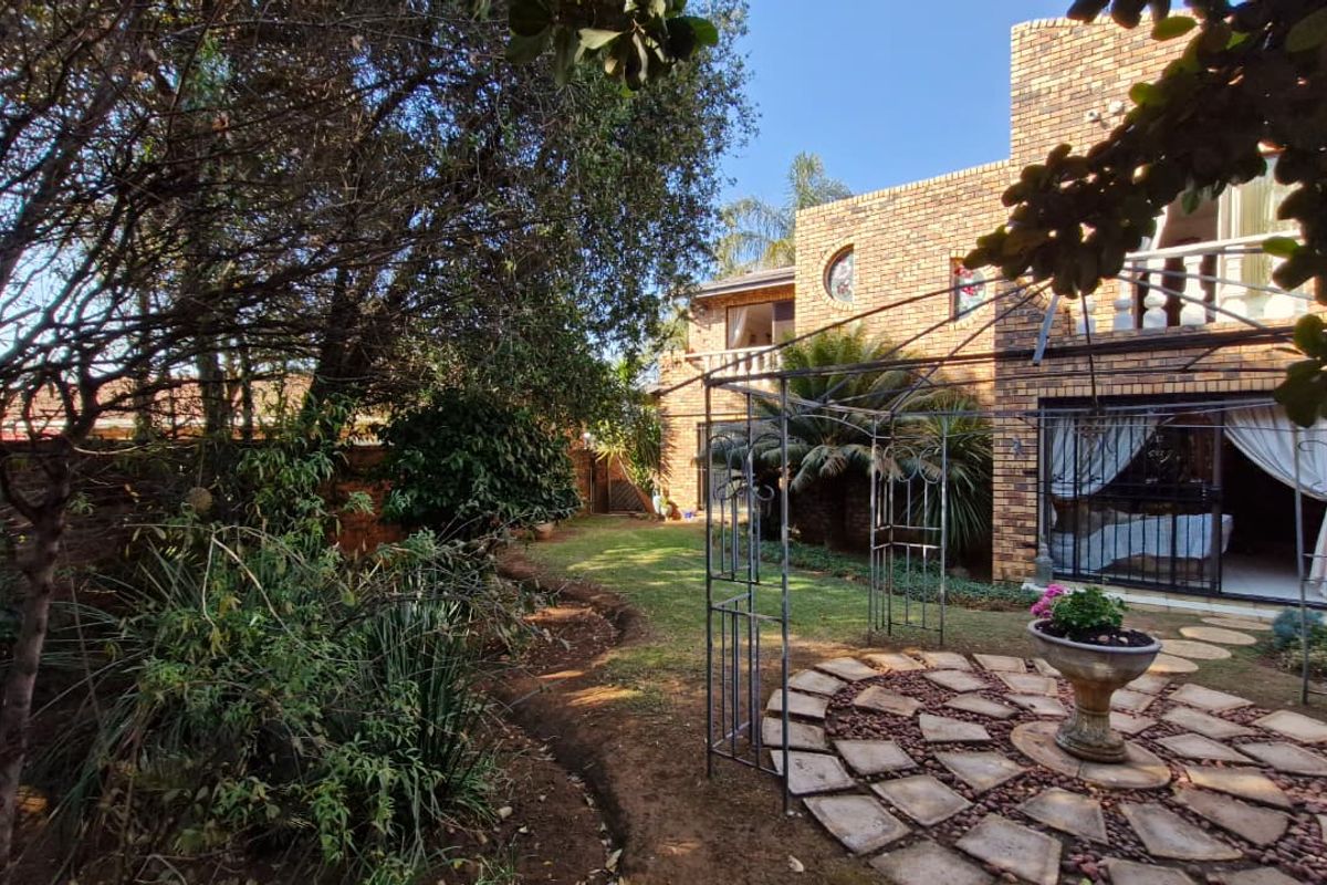 A private rear garden featuring a face brick facade, a metal pergola over a stone paved patio, and established landscaping.