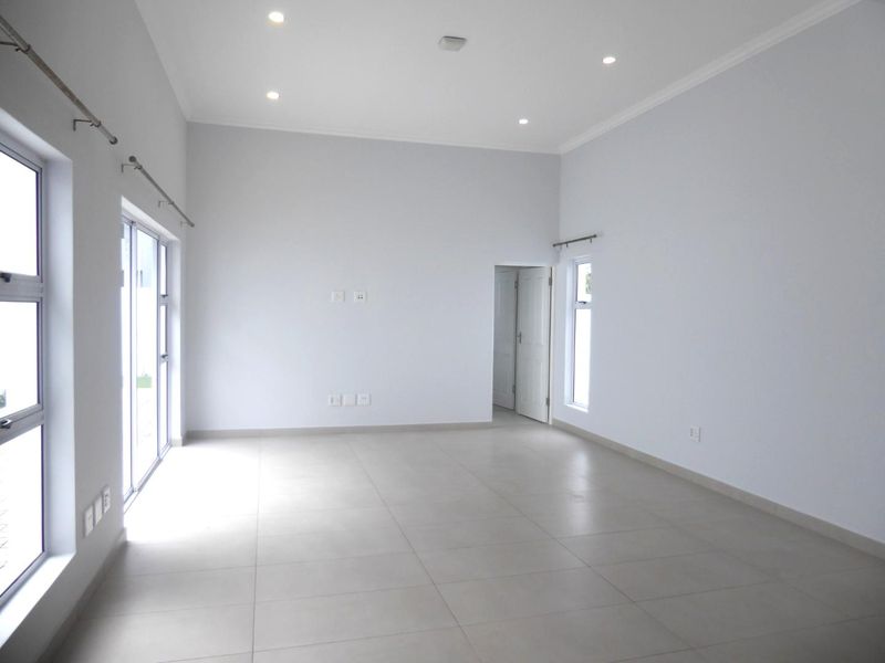 A bright, spacious, and empty living area featuring neutral tiled flooring, recessed downlights, and large sliding glass doors providing ample natural light.