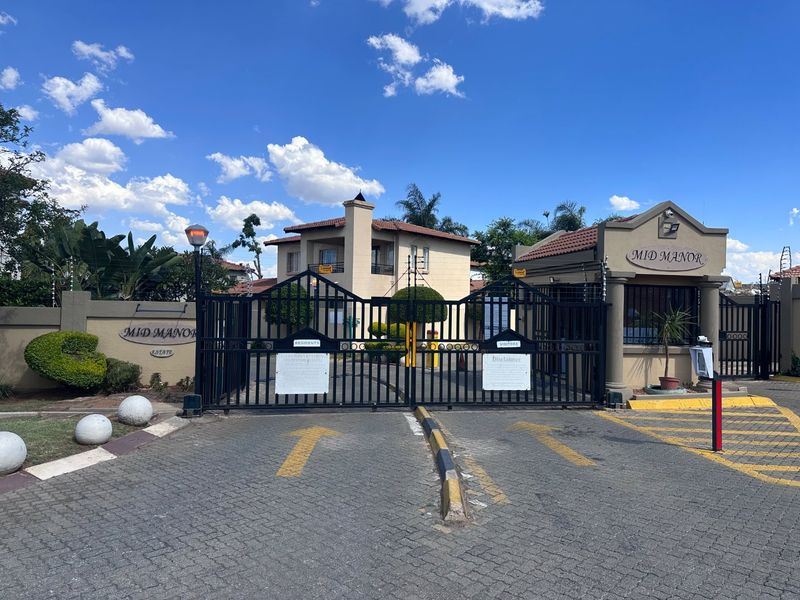 The secure entrance to Mid Manor Estate, featuring a gated access point, guard house, and paved driveway with perimeter security fencing.