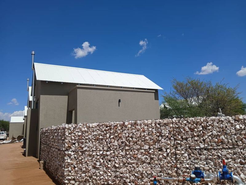 Rear view of the townhouse featuring a modern corrugated metal roof and a decorative stone gabion boundary wall with visible water utility connections.