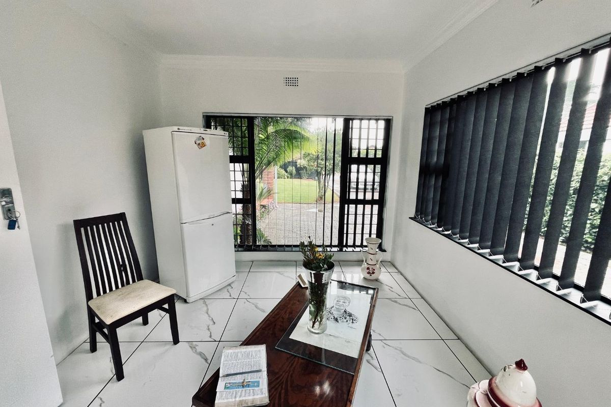 A bright living area featuring large windows with vertical blinds, marble-look tiled flooring, and a clean, neutral aesthetic.