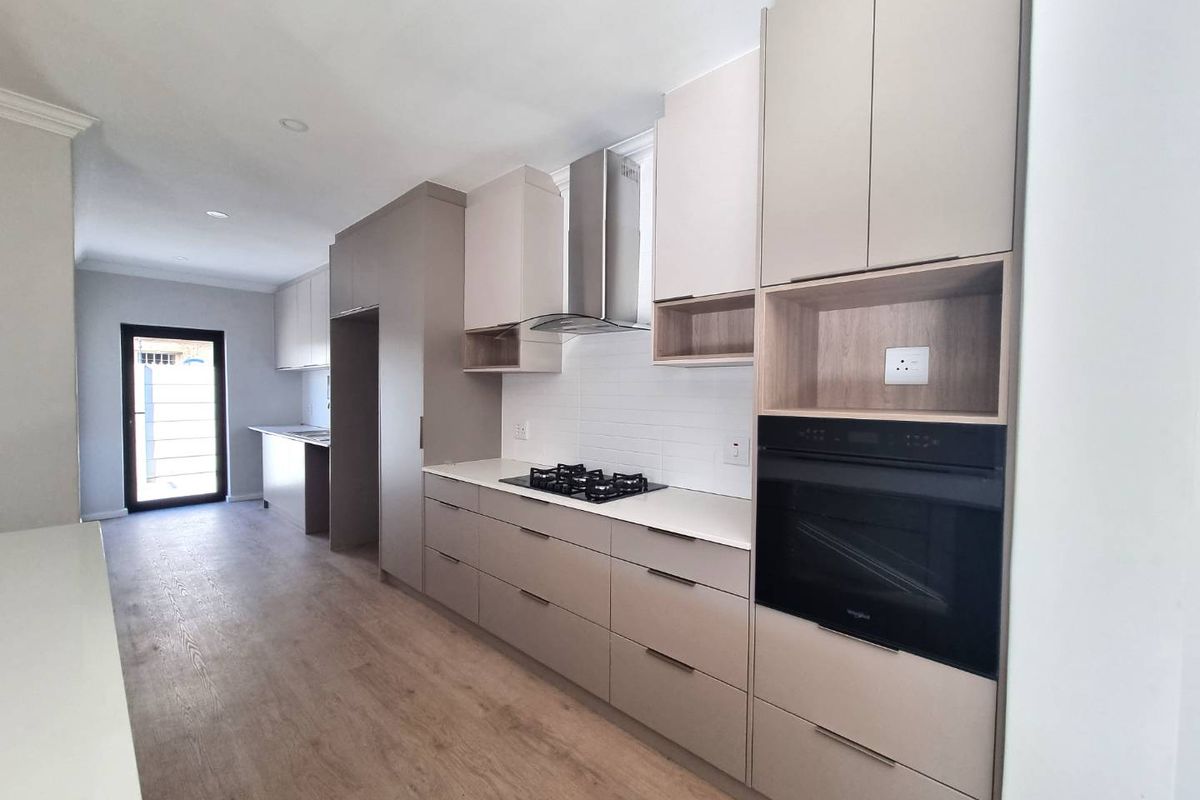 Modern kitchen featuring sleek built-in cabinetry, stone countertops, gas hob, extractor fan, and integrated oven with light wood-look laminate flooring.