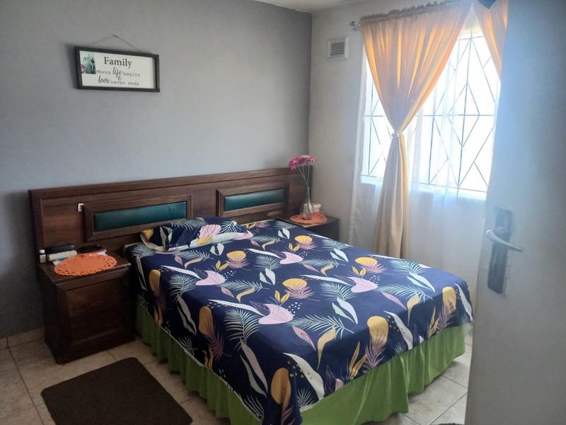 A functional bedroom featuring tiled flooring, a built-in headboard, and a window fitted with a security gate.
