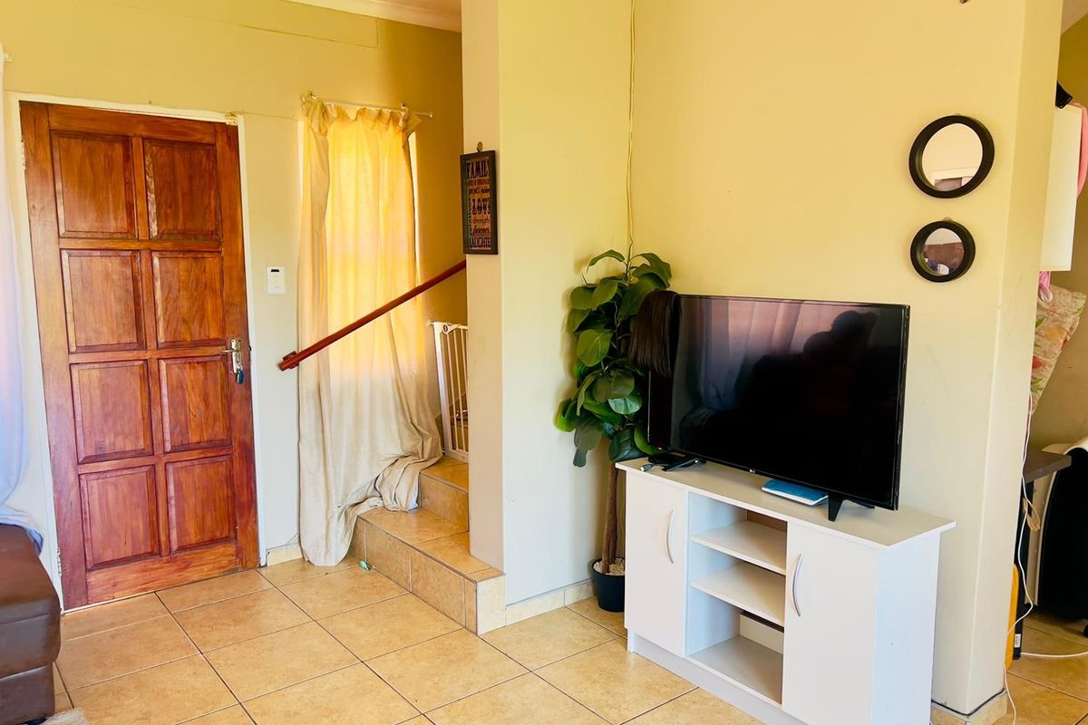 A living area featuring tiled flooring, a wooden entrance door, and a staircase with a handrail.