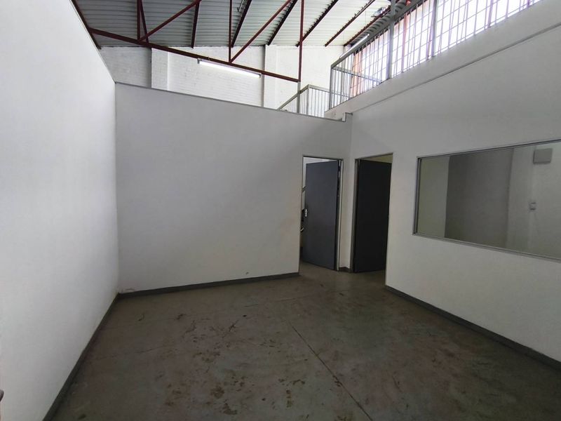 An industrial utility space featuring high ceilings with exposed steel trusses, a mezzanine level, and concrete flooring, suitable for storage or workshop use.