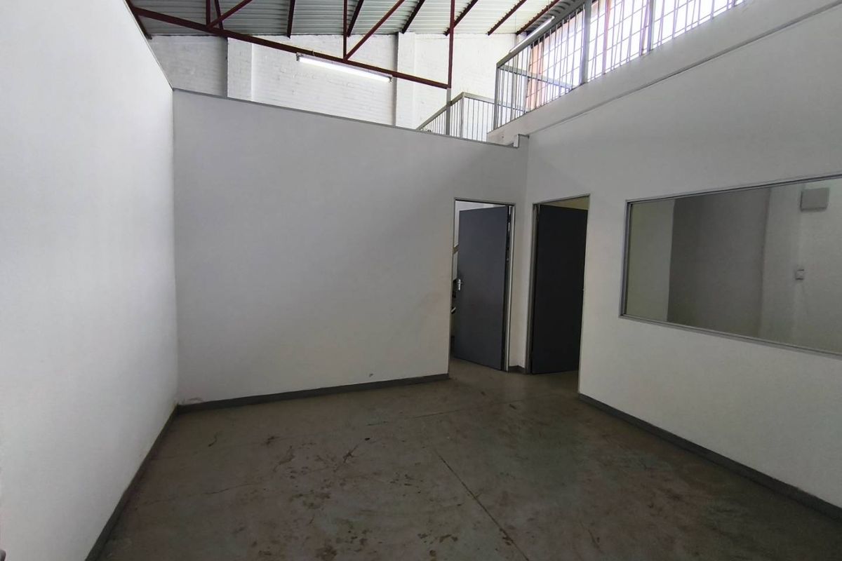 An industrial utility space featuring high ceilings with exposed steel trusses, a mezzanine level, and concrete flooring, suitable for storage or workshop use.