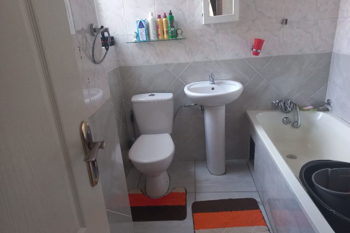 A functional bathroom featuring a pedestal sink, standard toilet, and a built-in bathtub with tiled walls and flooring.