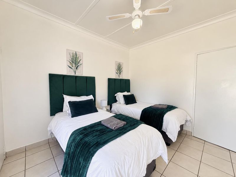 A clean and well-maintained bedroom featuring neutral tiled flooring, coved cornicing, and a central ceiling fan.