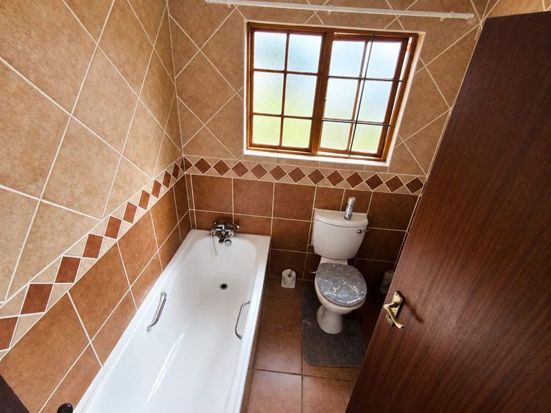 A compact bathroom featuring a bathtub, toilet, and classic brown tiled walls with a decorative border.