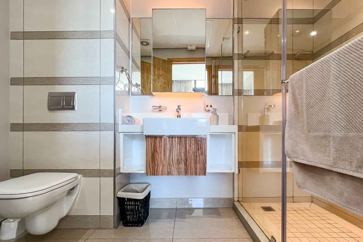 Modern bathroom featuring a wall-mounted toilet, floating vanity with integrated basin, and a glass-enclosed walk-in shower with tiled finishes.