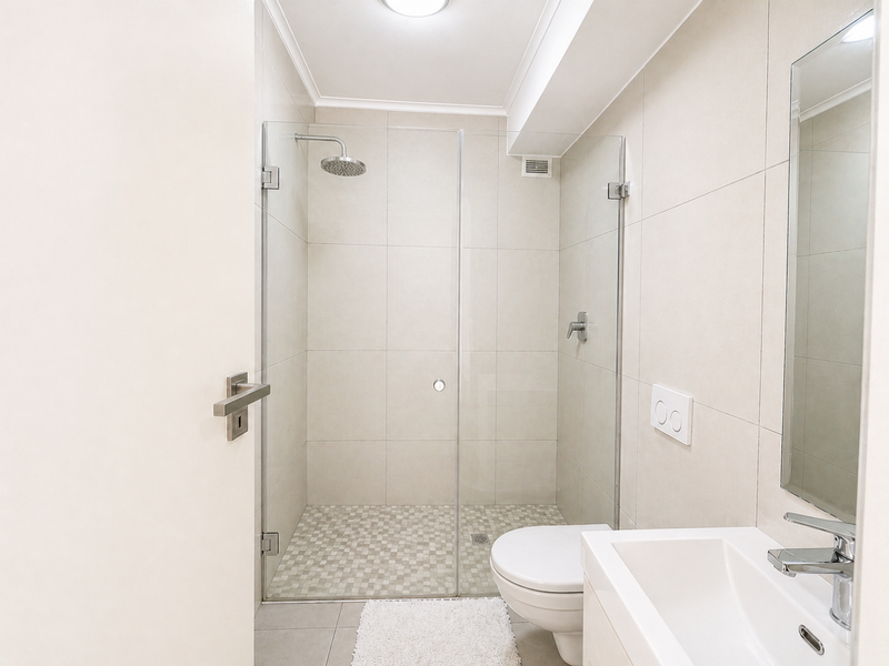 Modern bathroom featuring a walk-in shower with glass screen, rain shower head, wall-mounted toilet, and a sleek vanity basin with mirror.