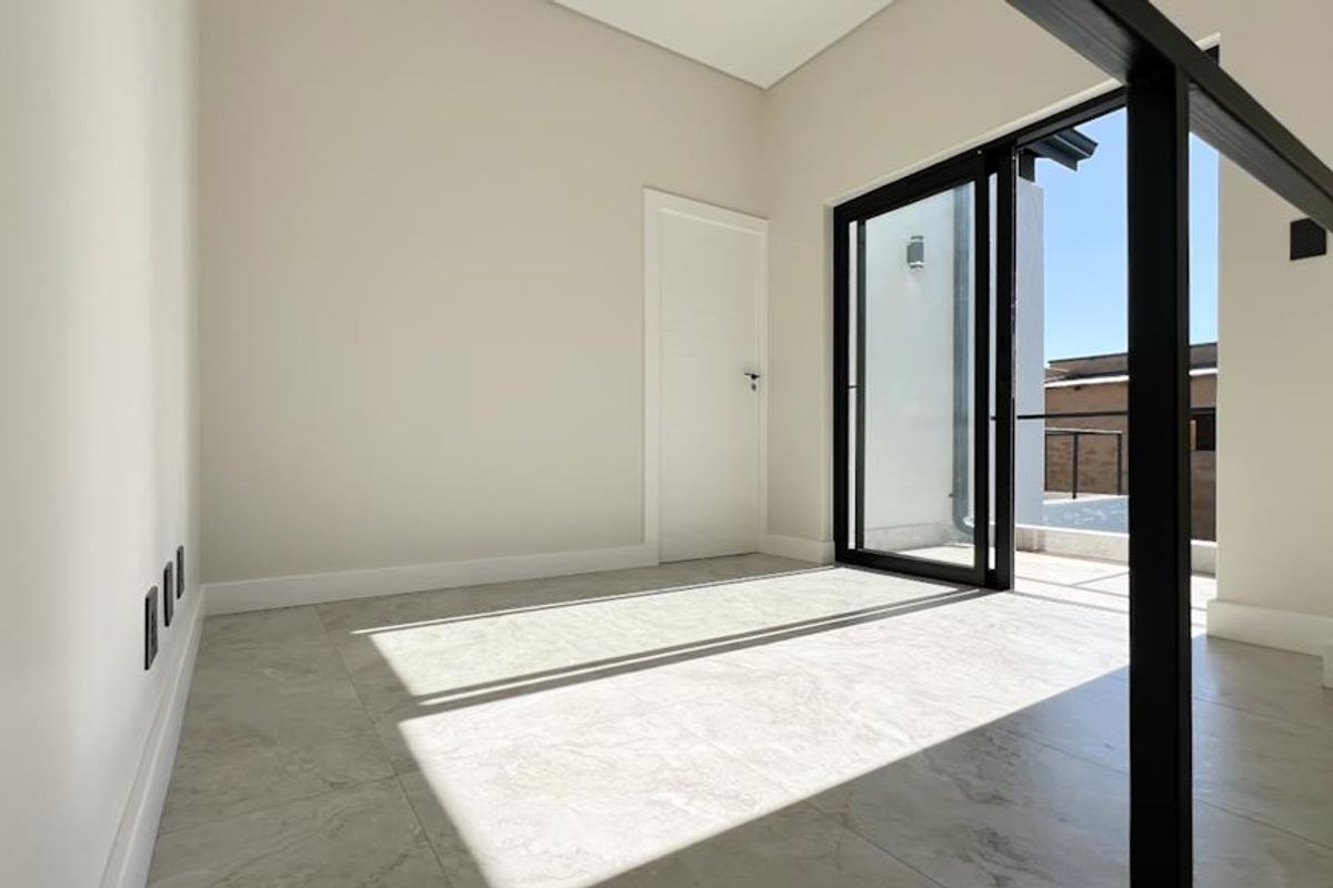 A bright, modern, and empty room featuring large sliding glass doors that open onto an outdoor balcony area.