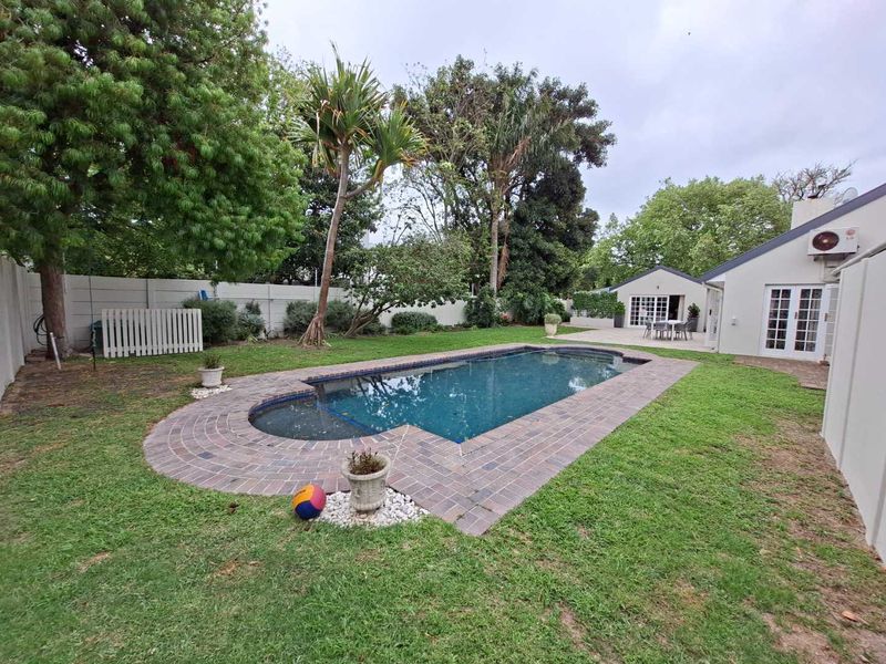 A well-maintained backyard featuring a swimming pool with brick paving, lush lawn, and direct access to the main house via french doors.