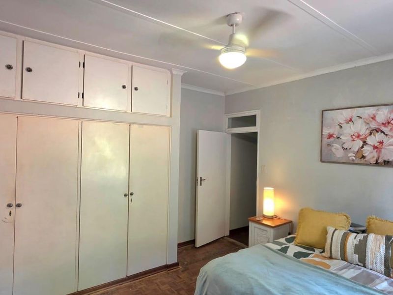 Bedroom featuring parquet flooring, a ceiling fan, and extensive built-in cupboard storage with overhead cabinets.