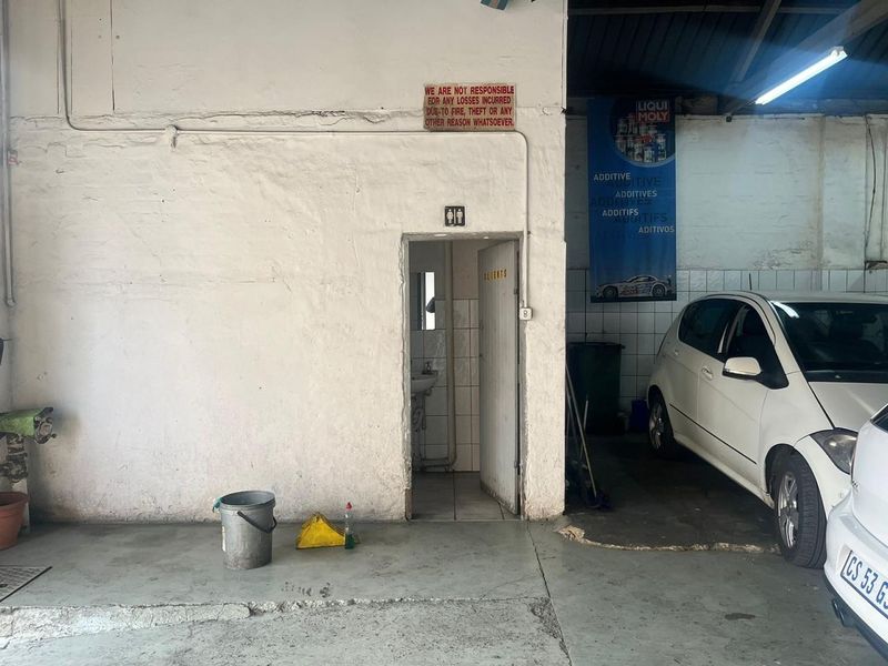 Industrial workshop area featuring a dedicated restroom facility with basic plumbing fixtures and concrete flooring, suitable for commercial or automotive operations.