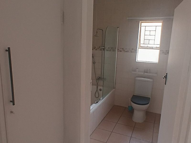 A functional bathroom featuring a bathtub with a glass shower screen, a toilet, and neutral wall and floor tiling.