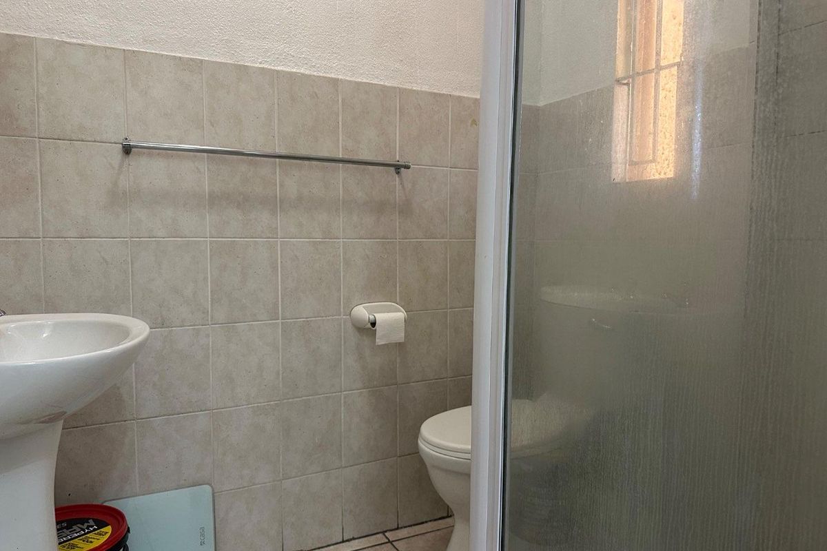 A functional bathroom featuring a pedestal basin, a toilet, and a glass-enclosed shower with neutral wall tiling.