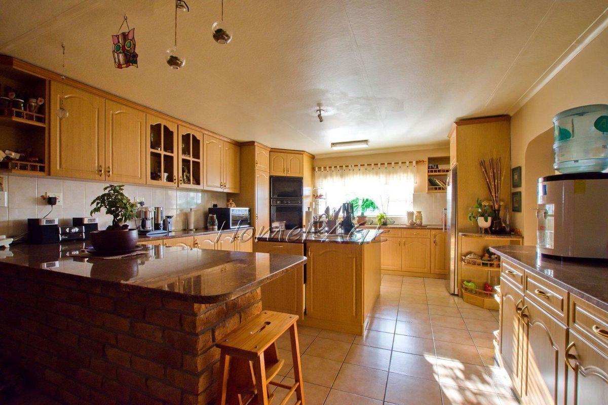 Spacious kitchen featuring light wood cabinetry, granite countertops, a central island, and built-in oven, offering a functional layout with tiled flooring.