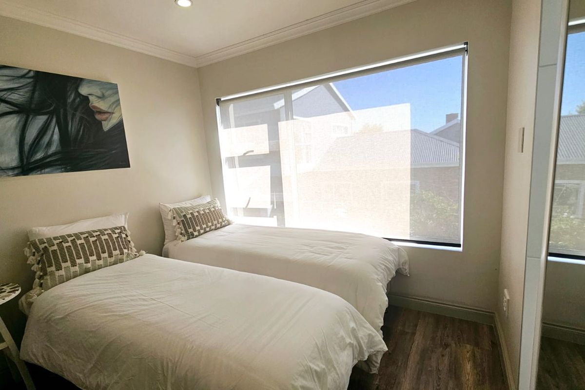 A bright bedroom featuring laminate flooring, a large window with a roller blind, recessed lighting, and a built-in wardrobe.