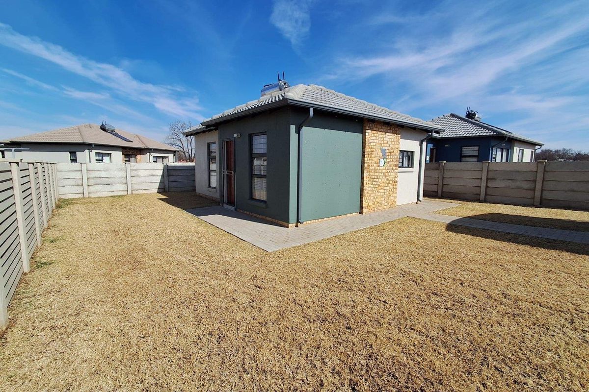 Rear view of the property featuring a well-maintained garden, paved pathways, and a solar water heating system installed on the tiled roof.