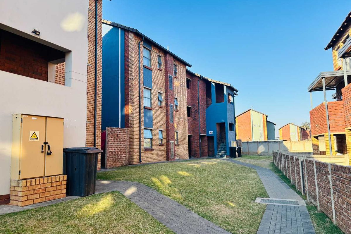 Exterior view of a multi-story apartment complex featuring brick facades, a landscaped lawn, and a paved pedestrian walkway.
