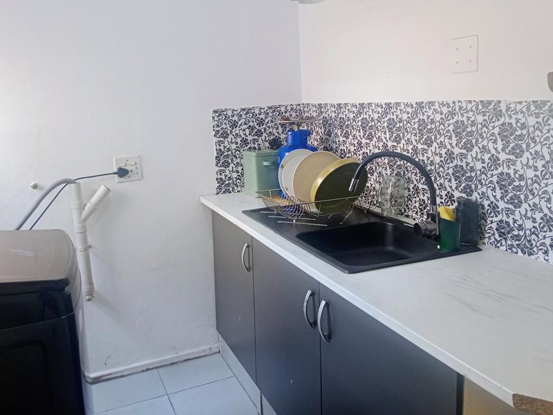 A functional laundry area featuring dark cabinetry, a white countertop, a black sink with a modern mixer tap, and a decorative patterned tile splashback.