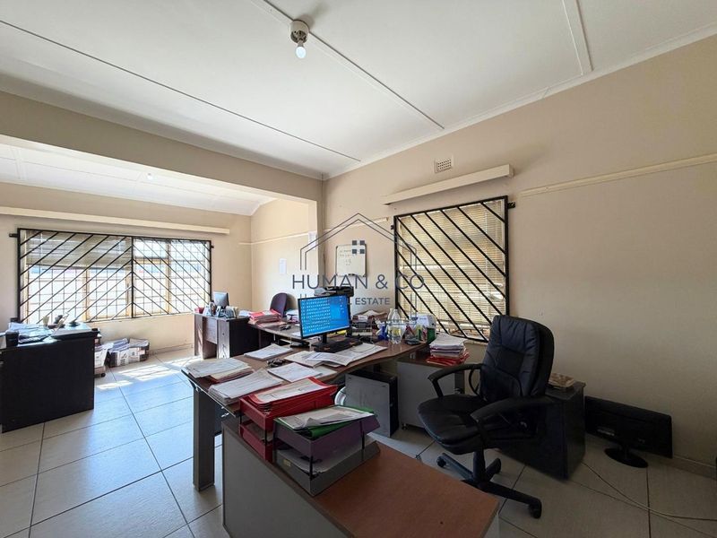 A functional office space featuring tiled flooring and large windows fitted with security bars, providing ample natural light for a professional work environment.