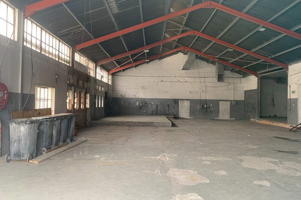 Spacious industrial warehouse unit featuring high ceilings with exposed steel trusses, concrete flooring, and large windows, suitable for various commercial or retail applications.