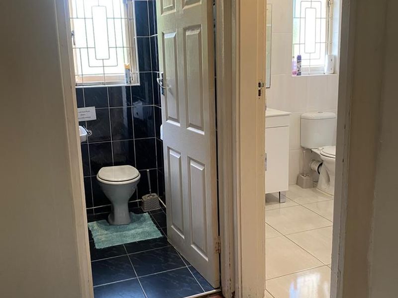 A view into two separate bathroom areas featuring tiled finishes, built-in toilets, and vanity units with security bars on the windows.