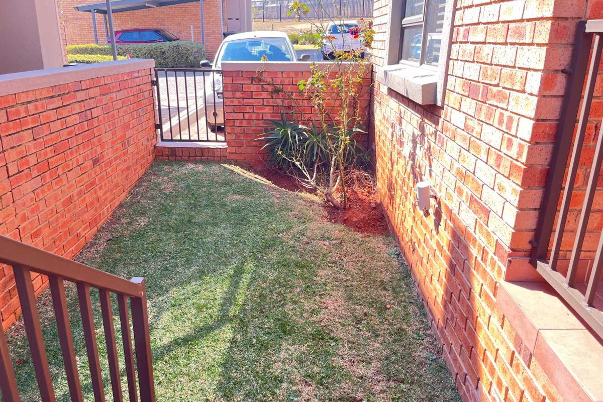 A small, private rear courtyard area featuring face brick walls, a metal gate, and a small patch of lawn.
