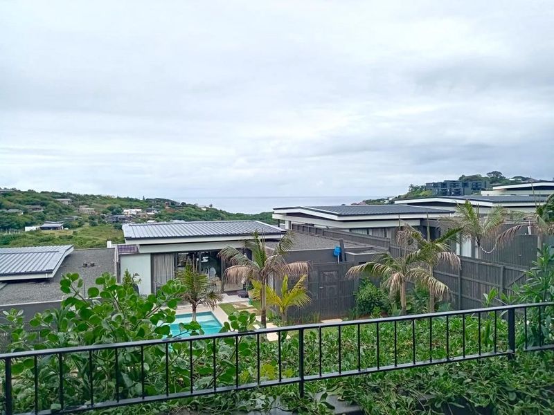 Elevated view overlooking a residential estate with swimming pool, modern townhouse architecture, and distant coastal scenery.