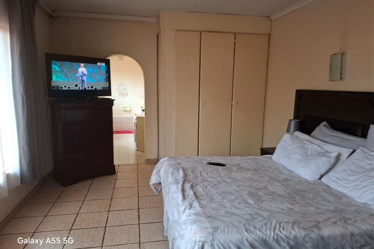 A bedroom featuring built-in cupboards and tiled flooring, with an arched doorway leading to an adjoining bathroom.