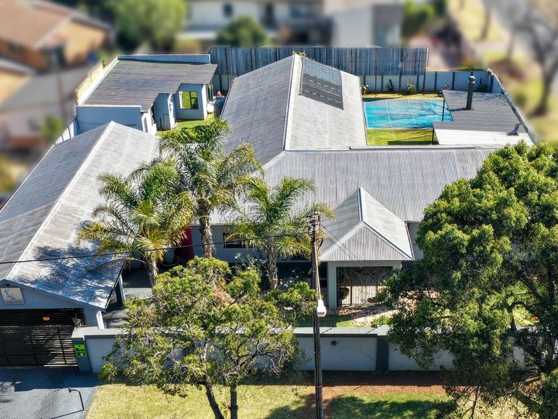 Aerial view of the property featuring a large corrugated metal roof with solar panels, a swimming pool with cover, and a secure perimeter wall.