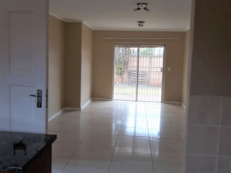 An empty, open-plan living area featuring neutral wall tones, tiled flooring, and a sliding glass door with security gate leading to the exterior.