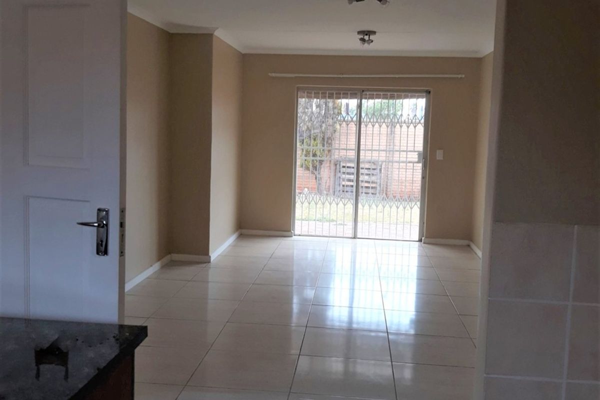 An empty, open-plan living area featuring neutral wall tones, tiled flooring, and a sliding glass door with security gate leading to the exterior.