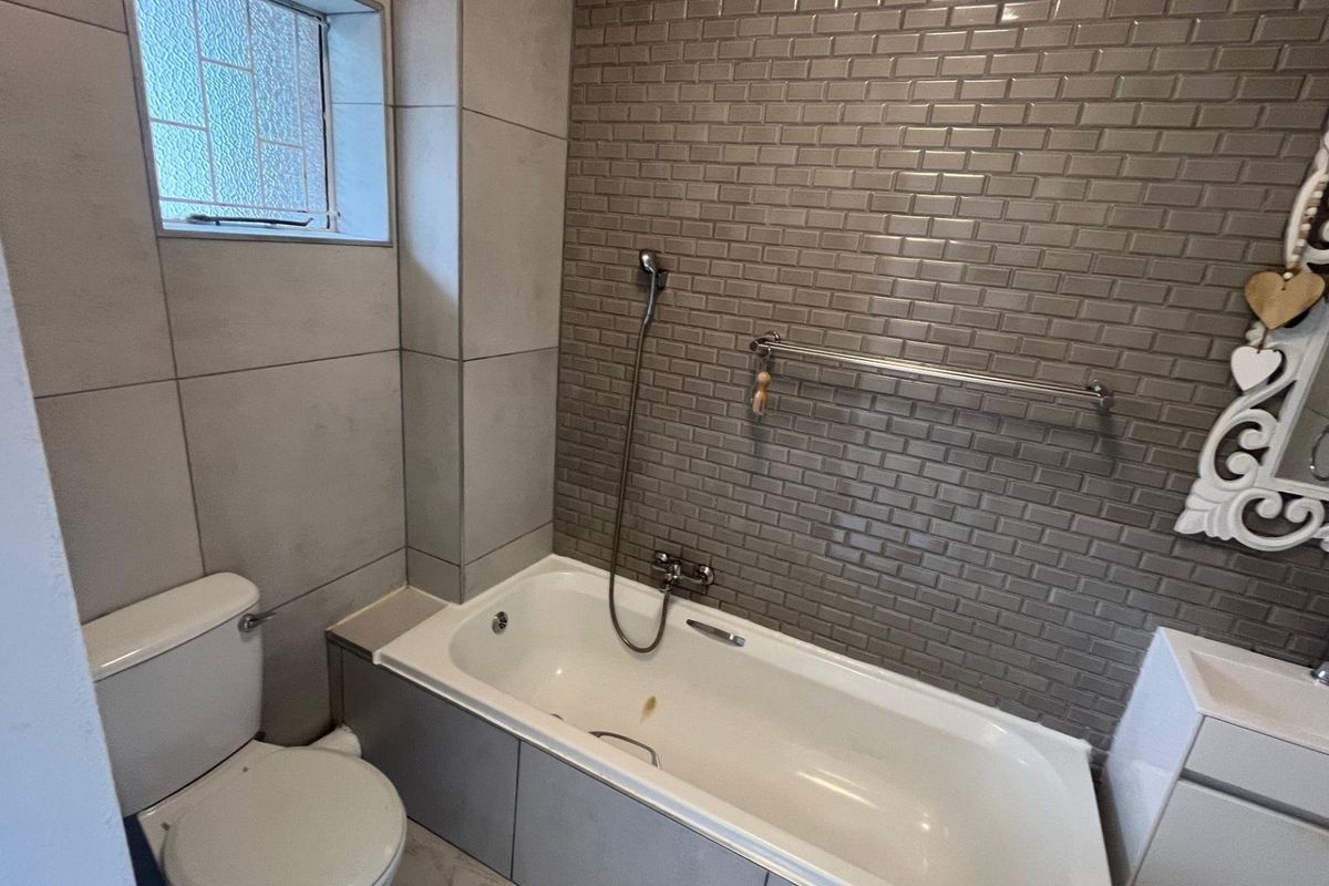 A functional bathroom featuring a bathtub with handheld shower, toilet, and vanity basin, finished with modern subway and large format wall tiling.