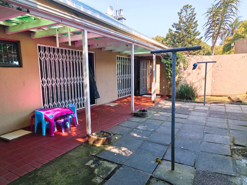 A covered rear patio area featuring tiled flooring, security gates, and an adjacent paved courtyard with a fixed washing line.