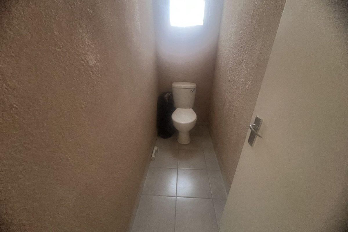 A small, functional toilet room featuring tiled flooring and a window, requiring cosmetic updates to the wall finishes.