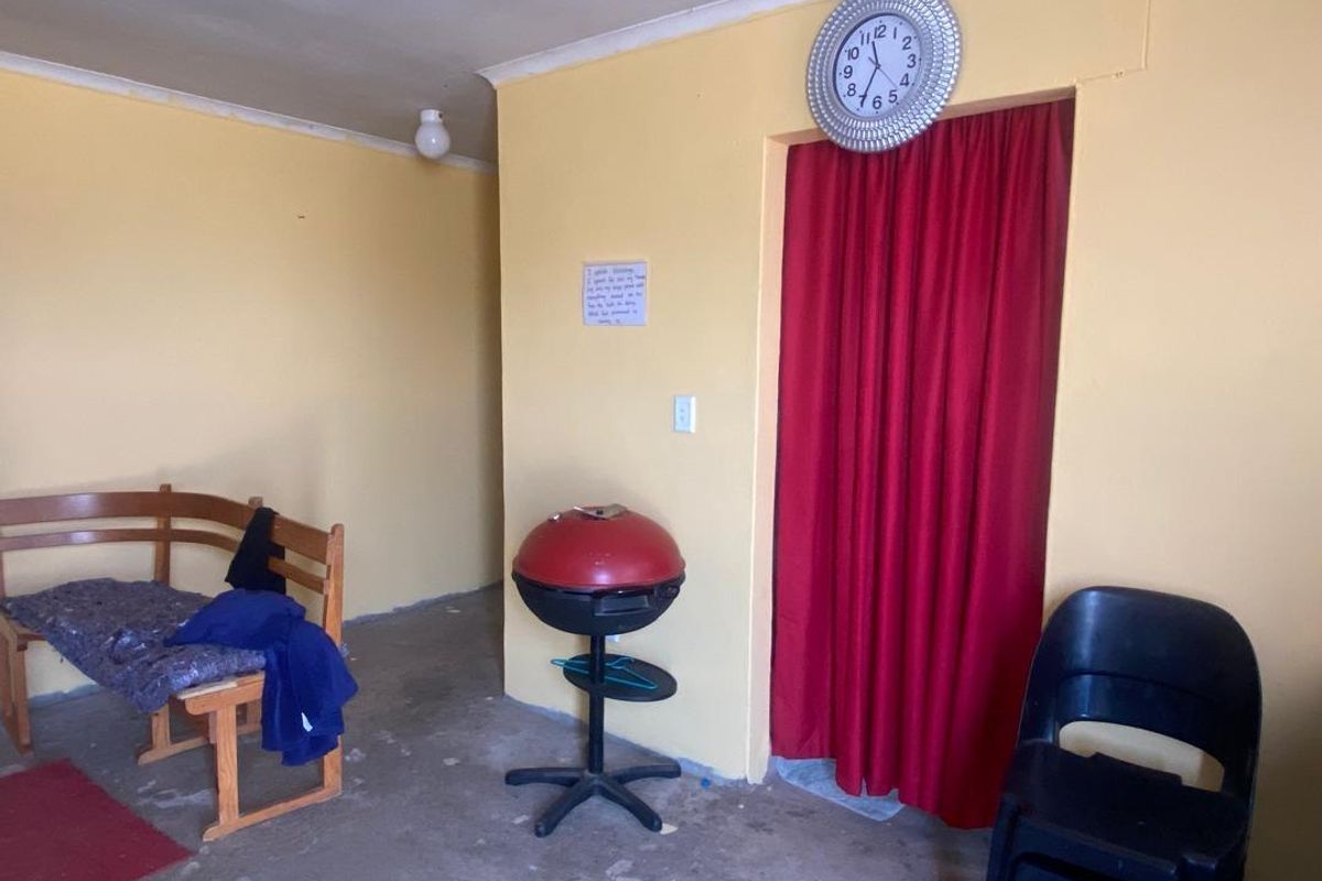 A sparsely furnished living area featuring yellow painted walls, cove cornicing, and an unfinished concrete floor.