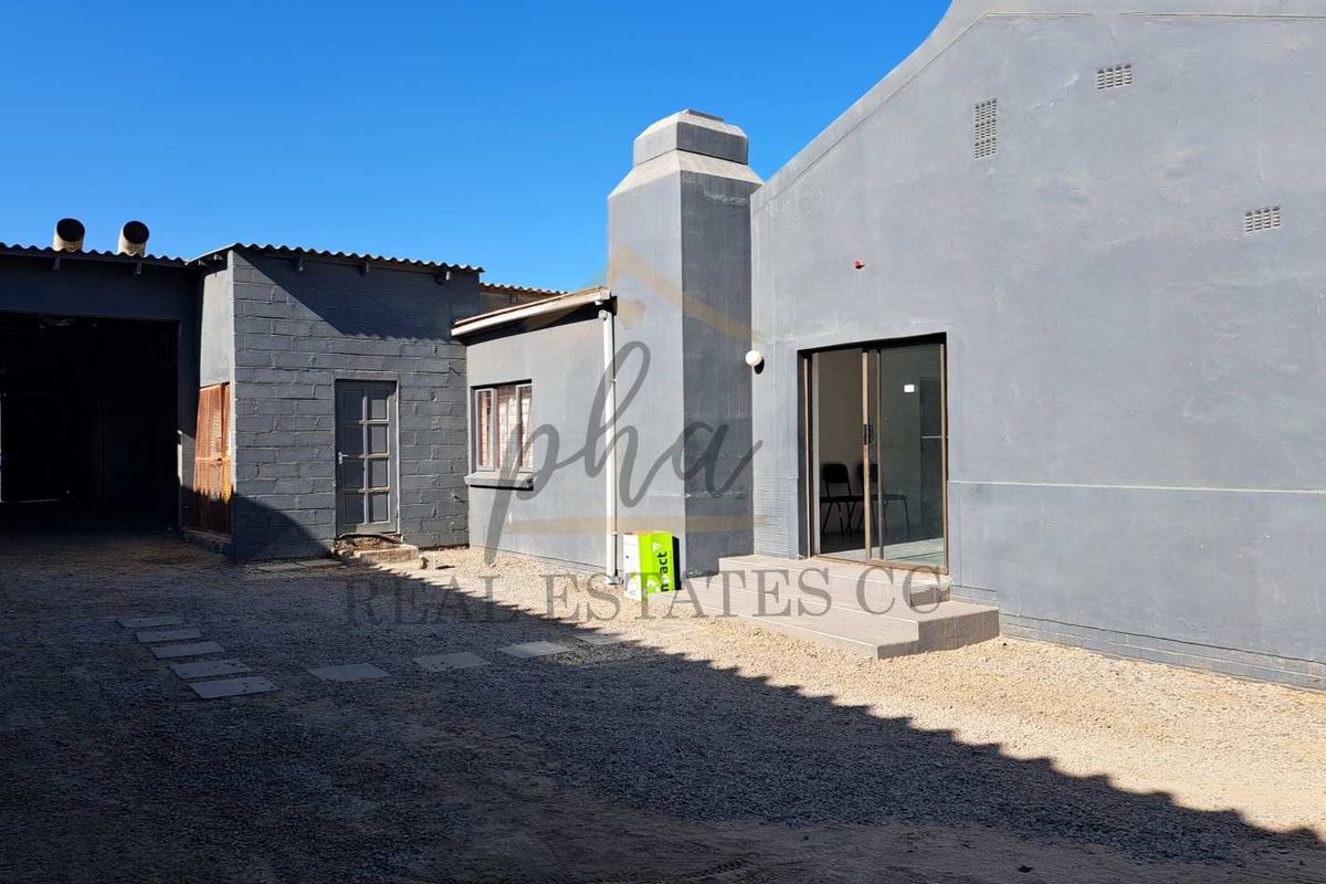 Rear exterior view of the property featuring a gravel courtyard, sliding glass door access, and a chimney stack.