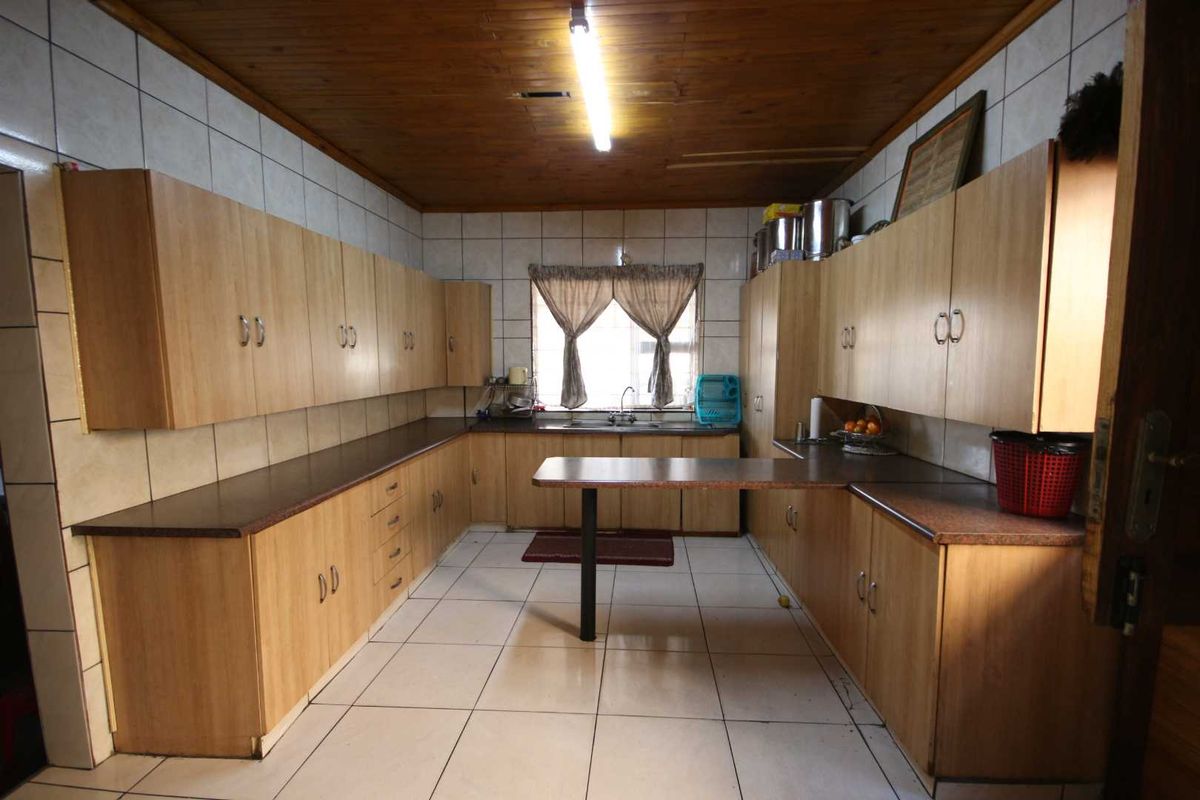 A functional kitchen featuring extensive laminate cabinetry, tiled surfaces, and a timber ceiling, offering a dated aesthetic with potential for modern renovation.