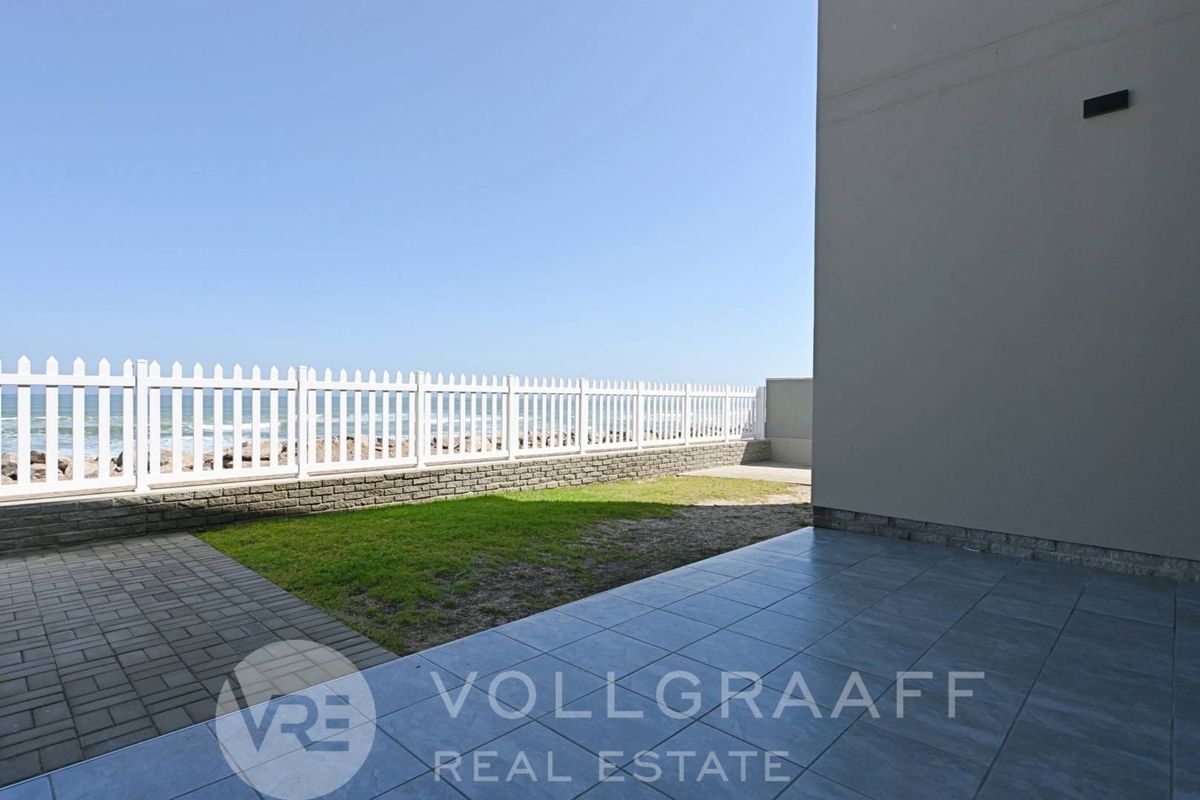 A private rear garden featuring a tiled patio area, a small lawn, and a white picket fence with direct ocean views.