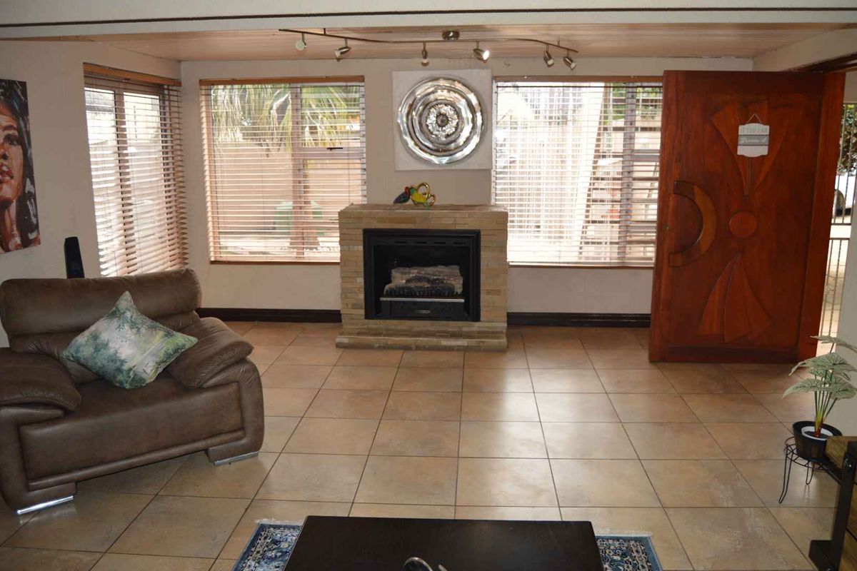 A living room featuring a central stone-clad fireplace, tiled flooring, and large windows with horizontal blinds, providing a functional and well-lit living space.