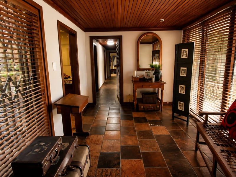 A well-maintained hallway featuring warm terracotta floor tiles, a timber slat ceiling, and large windows with timber blinds providing natural light.