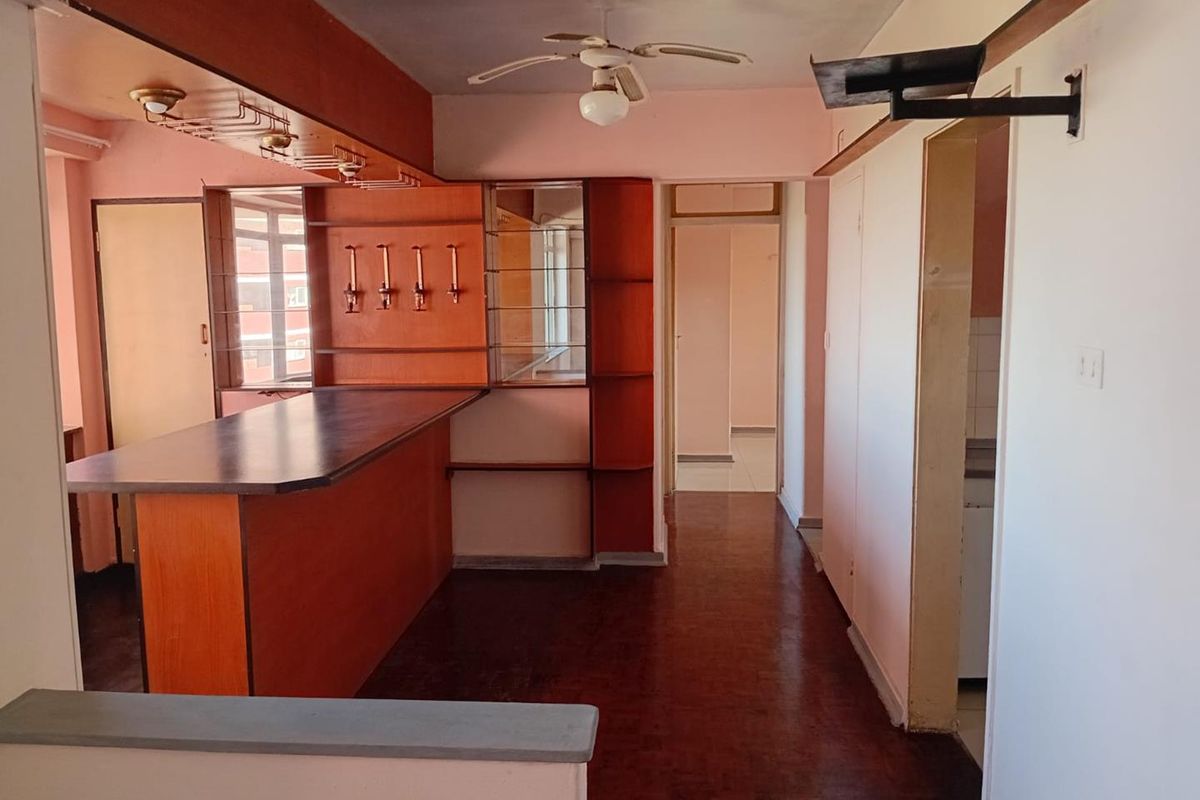 A dated living area featuring a built-in wooden bar counter, parquet flooring, and a ceiling fan, offering potential for modernization.