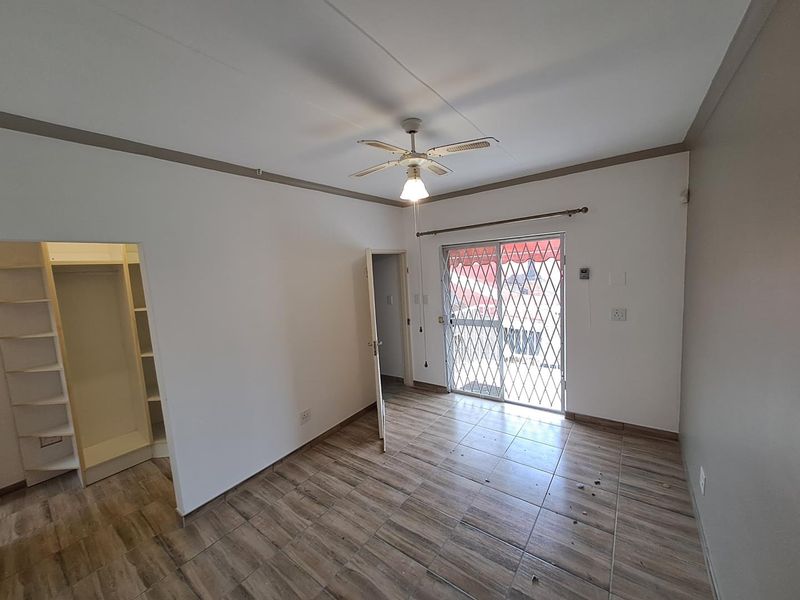 A vacant bedroom featuring tiled flooring, a built-in closet, a ceiling fan, and a sliding glass door with a security gate leading outside.