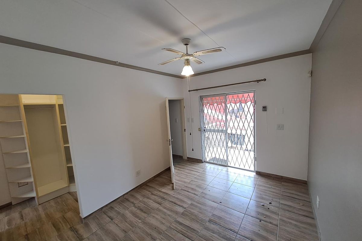 A vacant bedroom featuring tiled flooring, a built-in closet, a ceiling fan, and a sliding glass door with a security gate leading outside.