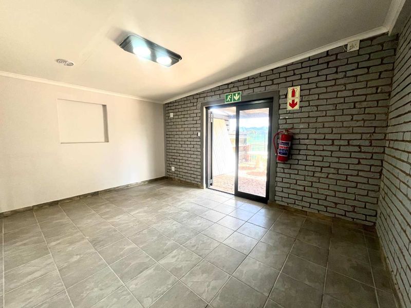 A clean, empty utility space featuring exposed brick walls, tiled flooring, and a sliding glass door providing access to the exterior.